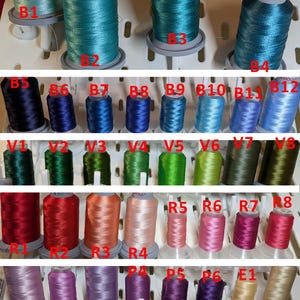 May include: A selection of embroidery thread spools in a variety of colours, such as black, white, gold, and silver. The image showcases shades of blue, green, red, pink, purple, yellow, and brown. The text "Merci de choisir la couleur de votre broderie" is present.