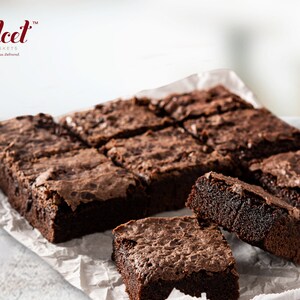 May include: A close-up of a tray of freshly baked chocolate brownies. The brownies are arranged in a grid pattern and are a rich, dark brown color. The brownies are on a white parchment paper.