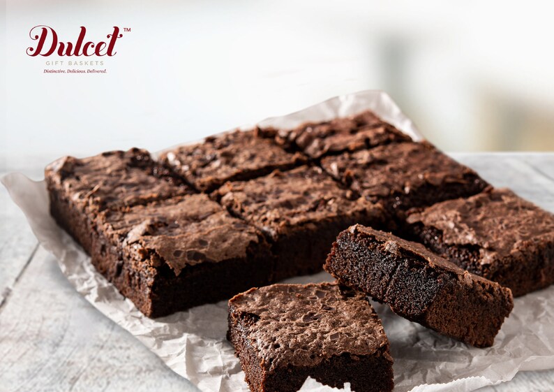 May include: A close-up of a tray of freshly baked chocolate brownies. The brownies are arranged in a grid pattern and are a rich, dark brown color. The brownies are on a white parchment paper.