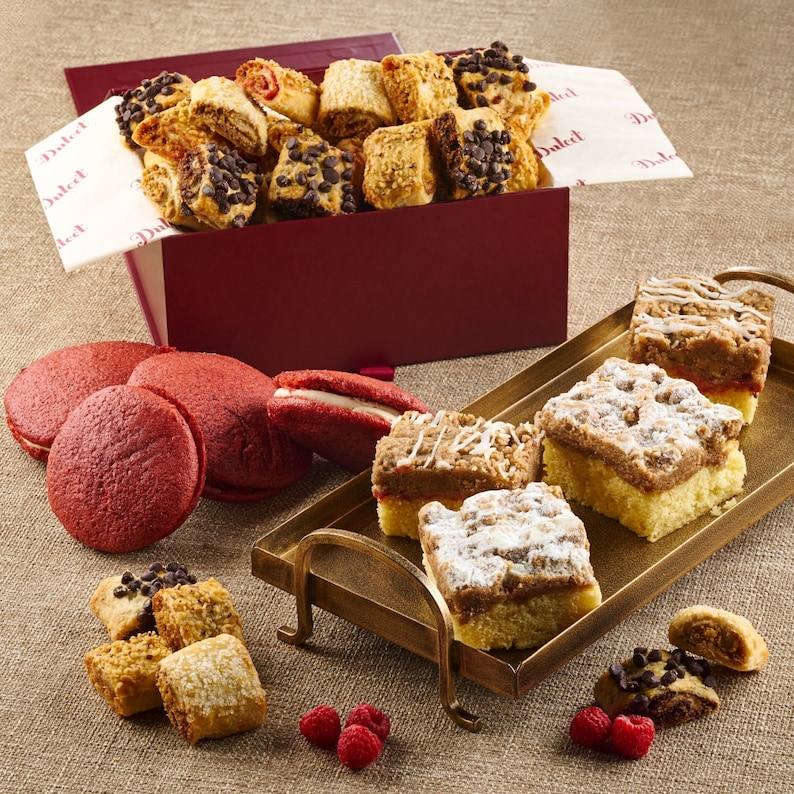 May include: A red box filled with assorted cookies, a tray with four crumb topped squares, and a variety of red velvet and other cookies. The box has the word "Dulcet" printed on the side.