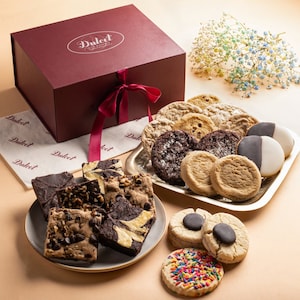 May include: A red gift box with a white ribbon and the text "Dulcet" on the top. The box is open and filled with a variety of cookies and brownies. The cookies include chocolate chip, sugar, and oatmeal raisin. The brownies are chocolate and fudge.