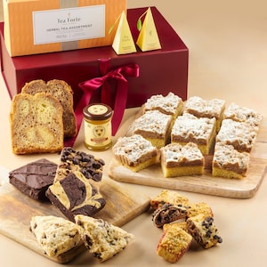 May include: A gift box filled with a variety of baked goods, including crumb cake, brownies, and shortbread cookies. The box is decorated with a red ribbon and a small jar of honey. The text on the box reads "Tea Forte Herbal Tea Assortment".