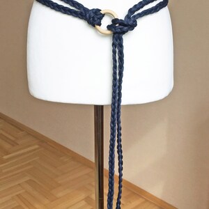 Peut inclure: Une ceinture en corde tress&eacute;e bleu marine avec un anneau en bois et des glands. La ceinture est nou&eacute;e autour d'un mannequin blanc.
