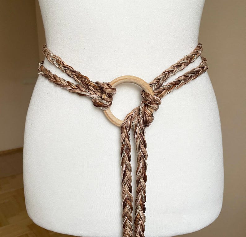 Peut inclure: Une ceinture en corde tress&eacute;e marron et blanche avec un anneau en bois. La ceinture est nou&eacute;e &agrave; l'avant et les extr&eacute;mit&eacute;s de la corde pendent.