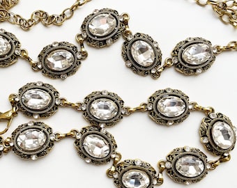 May include: A gold chain belt with oval-shaped clear rhinestones set in ornate frames. The belt is made of metal and has a delicate chain design.