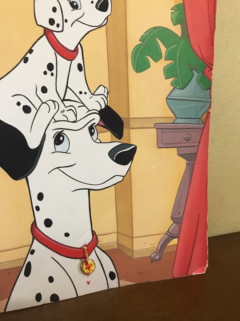 以下が含まれることがあります： 2匹のダルメシアンの犬の漫画イラスト。大きな犬は頭を横に傾けて立っており、小さな犬がその頭の上に座っています。両方の犬は赤い首輪に金のタグが付いています。