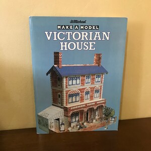 May include: A book cover with a blue background and the text "Make a Model Victorian House" in white. The cover features a detailed illustration of a Victorian house with red brick and white trim.