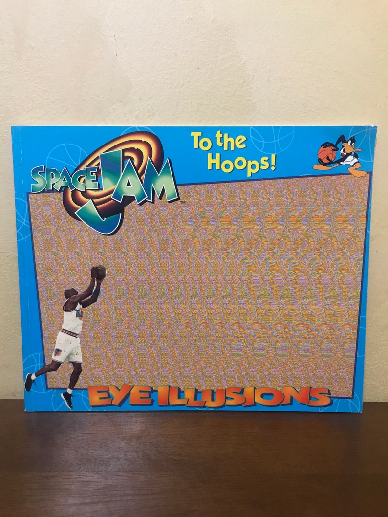 Pode incluir: Um livro azul e laranja do Space Jam com o texto "To the Hoops!" e "Eye Illusions" na capa. O livro apresenta uma imagem de desenho animado do Bugs Bunny jogando basquete.