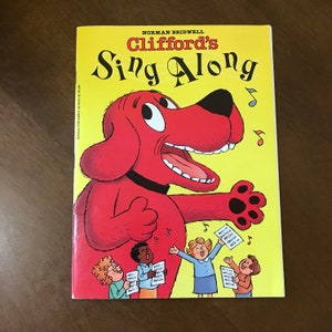 May include: A red dog with a big smile, singing with a group of children. The book cover says "Clifford's Sing Along" by Norman Bridwell.