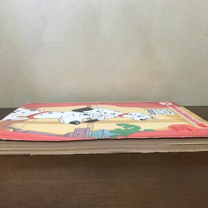 以下が含まれることがあります： ダルメシアンの漫画の画像が描かれた赤、白、黒の表紙の閉じた本。本は「101匹わんちゃん」というタイトルで、表紙に赤いステッカーが貼られています。