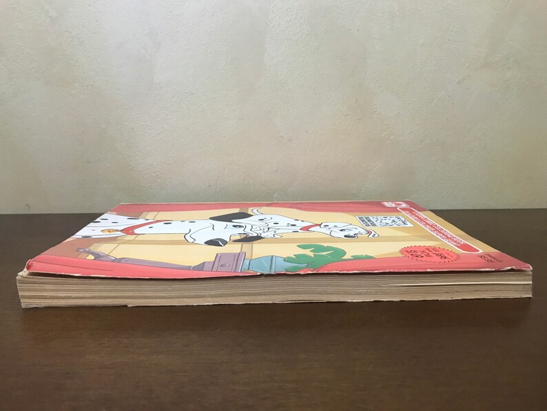 以下が含まれることがあります： ダルメシアンの漫画の画像が描かれた赤、白、黒の表紙の閉じた本。本は「101匹わんちゃん」というタイトルで、表紙に赤いステッカーが貼られています。
