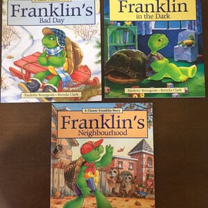 Peut inclure: Trois livres pour enfants mettant en sc&egrave;ne le personnage de Franklin la tortue. Le premier livre s'intitule "Franklin's Bad Day" et montre Franklin assis sur une luge dans la neige. Le deuxi&egrave;me livre s'intitule "Franklin in the Dark" et montre Franklin assis sur une chaise dans une pi&egrave;ce sombre. Le troisi&egrave;me livre s'intitule "Franklin's Neighbourhood" et montre Franklin marchant dans la rue avec un sac &agrave; dos.