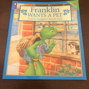 Peut inclure: Une tortue verte nomm&eacute;e Franklin tenant un chiot en peluche, regardant un chiot dans une cage. La couverture du livre indique "Franklin veut un animal de compagnie" et comporte le texte "Je suis &agrave; la t&eacute;l&eacute; !" dans un encadr&eacute; jaune.