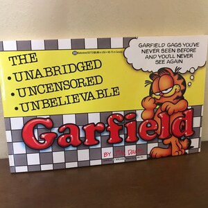 May include: A paperback book titled The Unabridged Uncensored Unbelievable Garfield by Jim Davis. The cover features a yellow background with a black and white checkered pattern at the bottom, an illustration of Garfield, and a speech bubble with text.