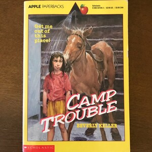 May include: A book cover for the novel "Camp Trouble" by Beverly Keller. The cover features a young girl in a red shirt and yellow shorts standing next to a brown horse being showered with water. The book is part of the Apple Paperbacks series.