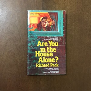 May include: A yellow and black book cover with the title "Are You in the House Alone?" by Richard Peck. The cover features a young woman looking out a window.