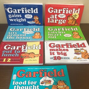 May include: A collection of seven Garfield comic books by Jim Davis, including titles such as Garfield Gains Weight, At Large, Sits Around the House, Eats His Heart Out, Out to Lunch, Makes It Big, and Food for Thought, featuring colorful covers.