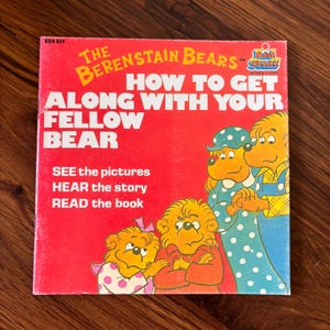 Peut inclure: Un livre pour enfants vintage intitulé "Les Ours en Peluche : Comment s'entendre avec votre camarade ours". La couverture est rouge avec des illustrations de personnages d'ours et le texte "Voir les images, Écouter l'histoire, Lire le livre."