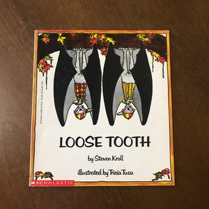May include: A children's book cover with a white background and a colorful illustration of two bats hanging upside down from a tree branch. The title of the book is "Loose Tooth" by Steven Kroll, illustrated by Tricia Tusa.