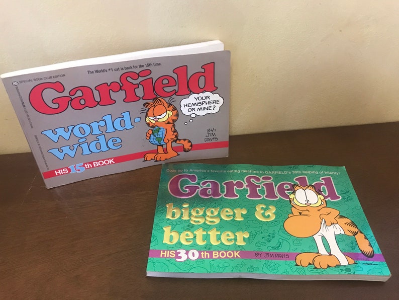 May include: Two Garfield comic books. The first book is titled Garfield worldwide, his 15th book, featuring an orange cat holding a globe. The second book is titled Garfield bigger & better, his 30th book, featuring an orange cat pulling up white underwear.