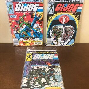 May include: Three comic books featuring the G.I. Joe characters. The covers are all different and feature different scenes from the comic book series. The first comic book is titled "G.I. Joe: A Real American Hero!" and features a tank with soldiers on top. The second comic book is titled "G.I. Joe: A Real American Hero!" and features a Cobra Commander helmet with Cobra soldiers inside. The third comic book is titled "G.I. Joe: A Real American Hero!" and features a group of G.I. Joe soldiers in a snowy landscape.