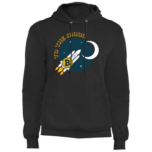 May include: Black hoodie with a graphic of a rocket ship with a Bitcoin symbol, launching towards a blue circle with a crescent moon and stars. The text "TO THE MOON" is arched above the circle.