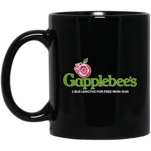 May include: A black ceramic mug featuring a logo with a red turbocharger icon topped by a green leaf. The text reads Gapplebee's in green letters, followed by the white text 2 BUS LENGTHS FOR FREE MON-SUN centered below the main brand name.