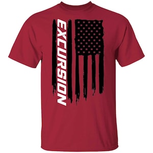 May include: A maroon short-sleeved t-shirt featuring a black graphic of a distressed American flag design. The word EXCURSION is printed vertically in bold white capital letters along the left side of the black flag graphic on the front.