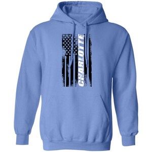 May include: A light blue hooded sweatshirt with a distressed American flag design and the word "CHARLOTTE" in white lettering.