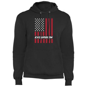 May include: Black hooded sweatshirt featuring a graphic of the American flag with red stripes and white stars. The word "EXCURSION" is printed in white block letters below the flag design. The sweatshirt has a drawstring hood and ribbed cuffs.