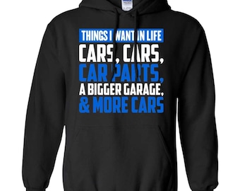 May include: A black hooded sweatshirt featuring white and blue text that reads: THINGS I WANT IN LIFE CARS, CARS, CAR PARTS, A BIGGER GARAGE, & MORE CARS. The garment includes a drawstring hood, long sleeves, and a front kangaroo pocket.