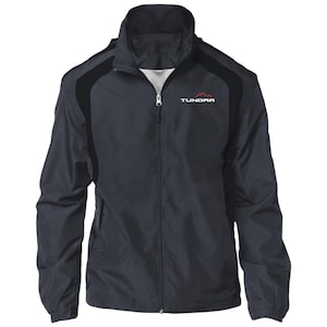 May include: A navy blue zip-up jacket with black shoulder accents. The jacket features the word "TUNDRA" in white text with a red mountain graphic. The jacket has a high collar and a full-length zipper.