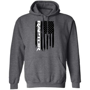 May include: A dark heather gray hooded sweatshirt featuring a vertical graphic on the chest. The graphic displays a distressed black and white American flag design with the word RAPTOR printed in white capital letters along the left side.