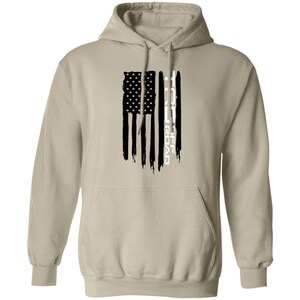 May include: A beige hooded sweatshirt featuring a black and white graphic on the front. The design depicts a distressed American flag with vertical stripes, incorporating the text TRD OFF ROAD in a vertical orientation within the flag's design.