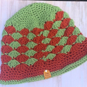 May include: Green and brown crocheted hat with a diamond pattern. The hat has a leather tag that says "Calypso Peacock by Kristie".
