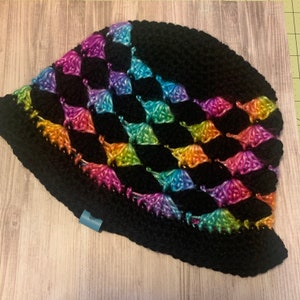 May include: A black crochet hat with a rainbow diamond pattern. The hat is made with a soft, textured yarn.