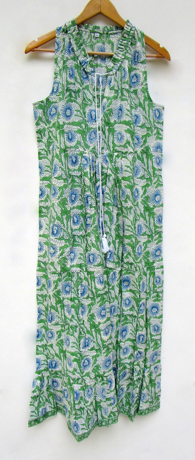 May include: A sleeveless green and white dress with a blue floral print. The dress has a ruffled neckline and a drawstring tie at the front.