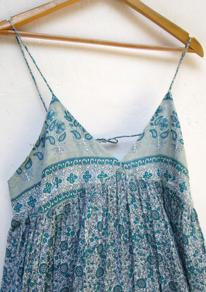 May include: A light blue and white floral print sleeveless dress with a V-neck and thin straps. The dress has a gathered skirt and a tie at the back of the neck.