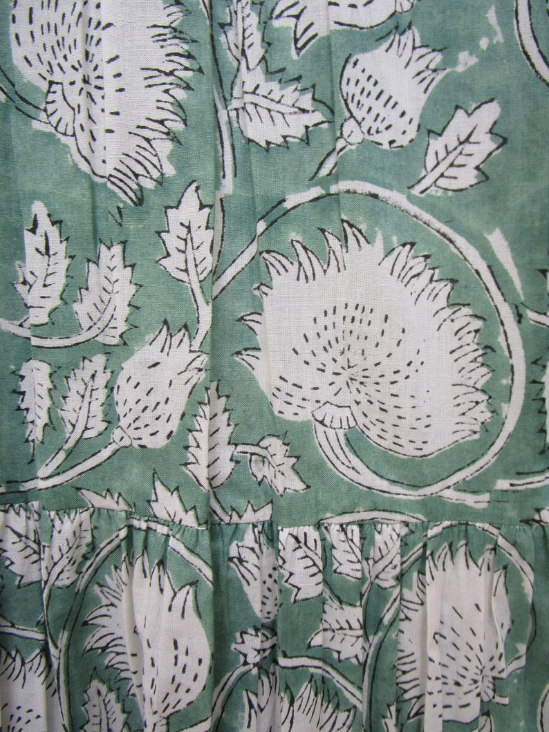 May include: Close-up of a fabric with a repeating floral pattern. The design features large white flowers and leaves with black outlines against a muted green background. The fabric has a textured appearance.