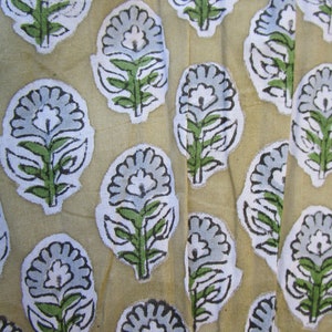 May include: A beige fabric with a repeating pattern of blue and white floral designs. The flowers have a stylized look with green leaves and stems.