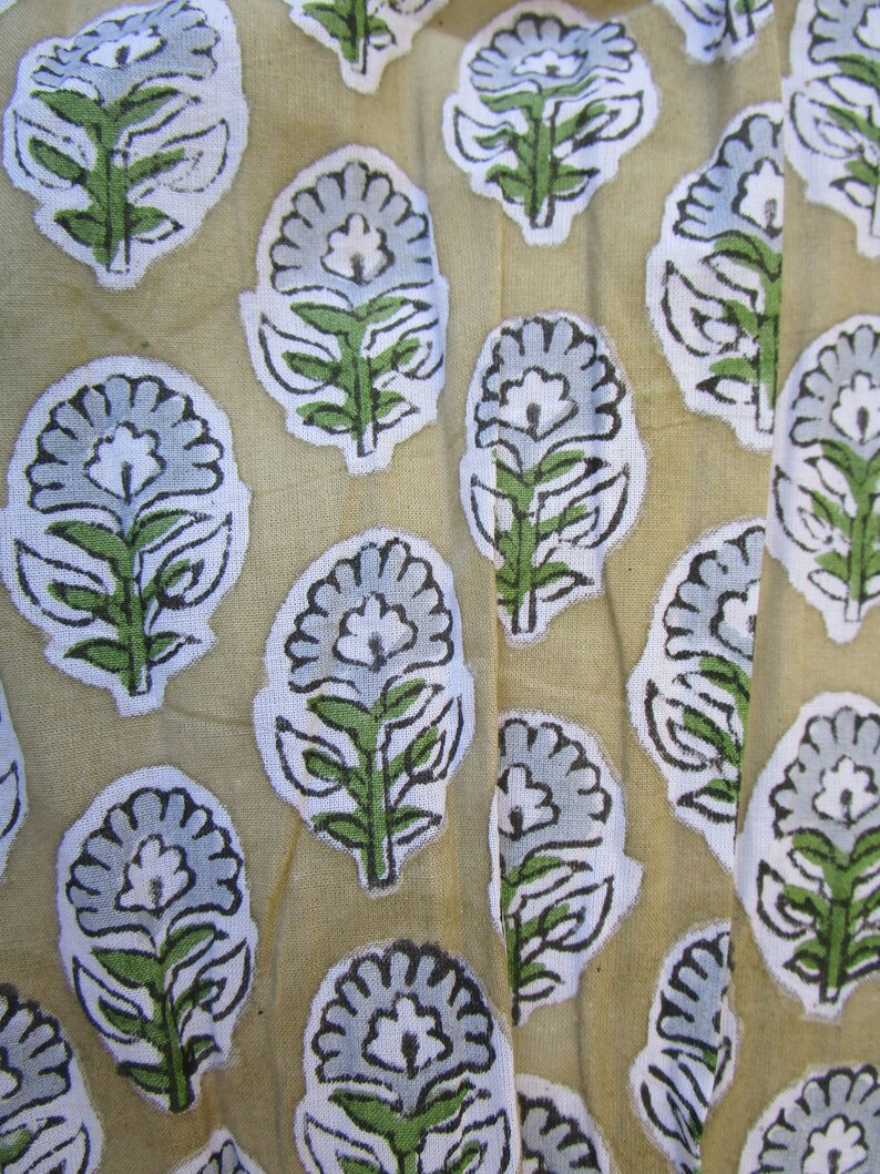 May include: A beige fabric with a repeating pattern of blue and white floral designs. The flowers have a stylized look with green leaves and stems.