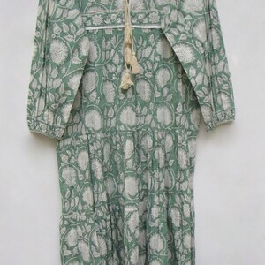 May include: A long, green dress with a white floral print. It has long sleeves, a V-neck with a tassel tie, and a tiered skirt. The dress is made of a lightweight fabric, ideal for warmer weather. The measurements are in centimetres.