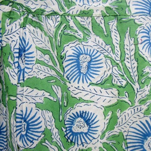 May include: Green fabric with a white and blue floral pattern. The flowers have a blue center and white petals with blue lines radiating out from the center.