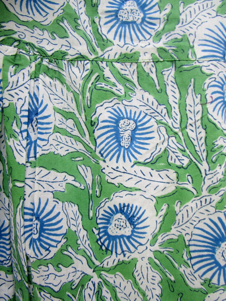 May include: Green fabric with a white and blue floral pattern. The flowers have a blue center and white petals with blue lines radiating out from the center.