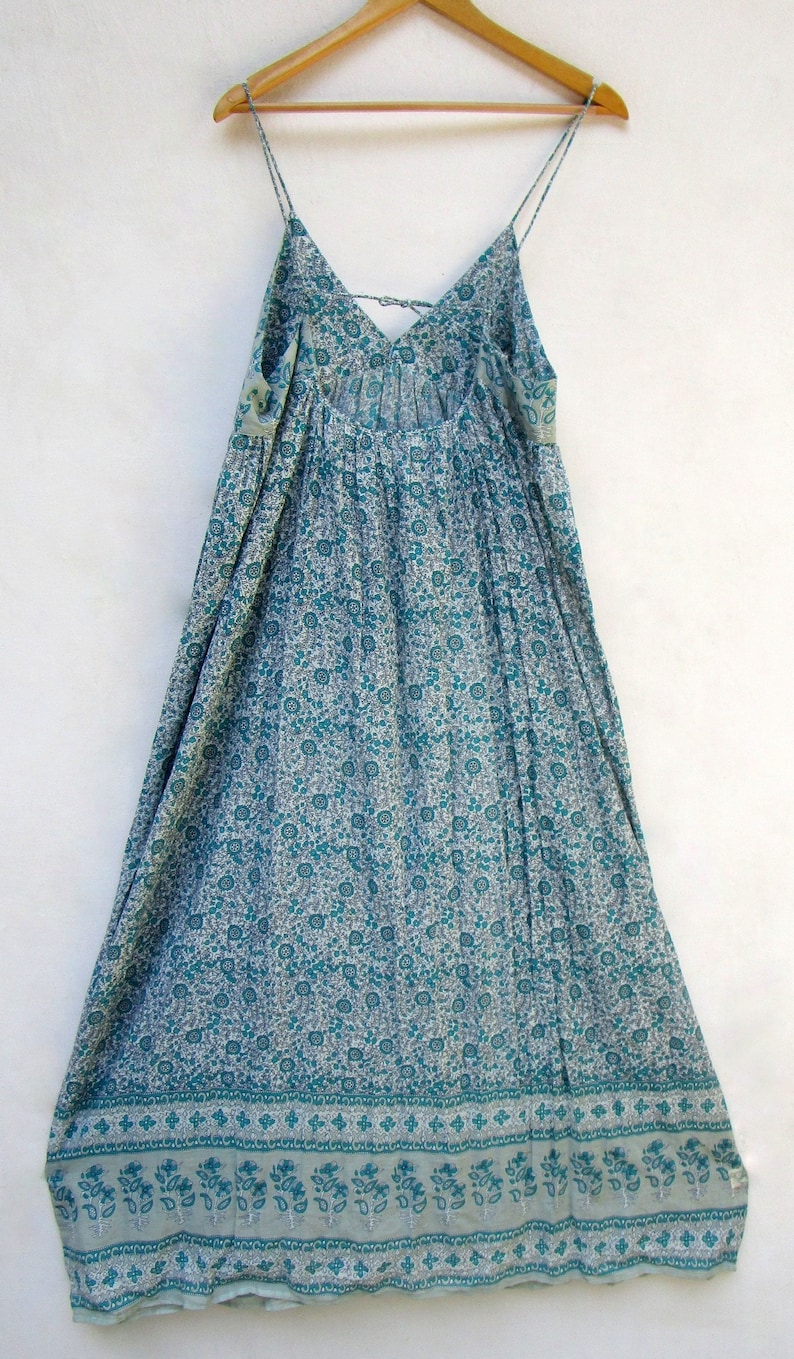 May include: A long, light blue maxi dress with a floral print. The dress has thin straps and a V-neckline. The hem of the dress has a decorative border.
