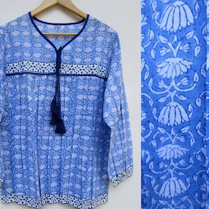 May include: A blue cotton tunic top with a white floral print and a navy blue tassel tie. The top has a V-neck and long sleeves.