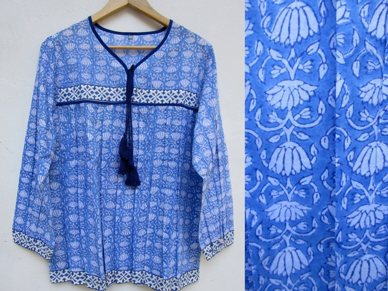 May include: A blue cotton tunic top with a white floral print and a navy blue tassel tie. The top has a V-neck and long sleeves.