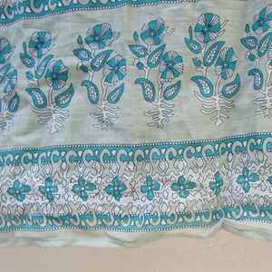 May include: A close-up of a light blue fabric with a white and teal floral pattern. The fabric has a repeating design of flowers, leaves, and paisley shapes.