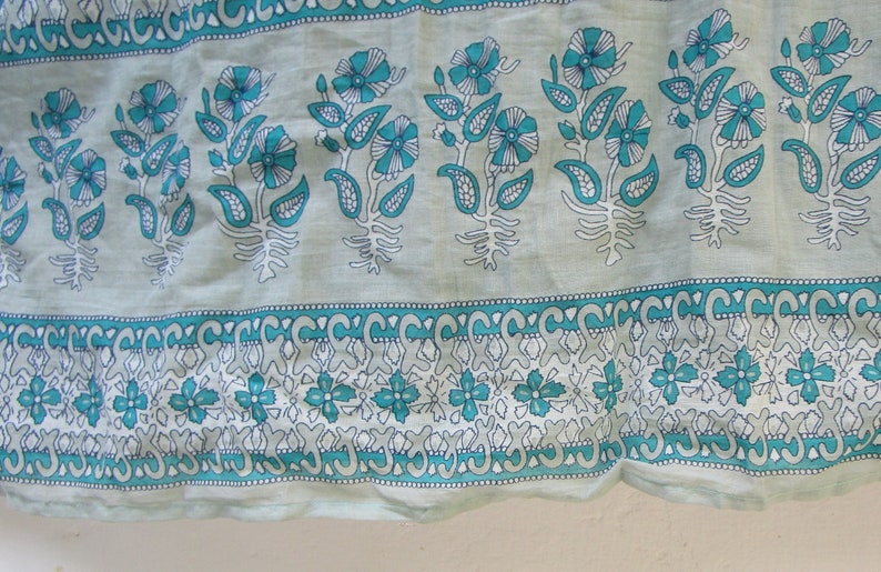 May include: A close-up of a light blue fabric with a white and teal floral pattern. The fabric has a repeating design of flowers, leaves, and paisley shapes.