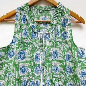 May include: A sleeveless green cotton top with a white and blue floral print. The top has a ruffled neckline and a drawstring closure.